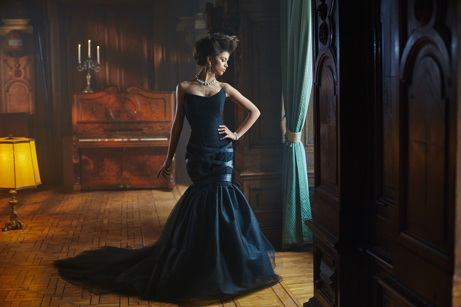 A woman in a black dress is standing in a room next to a piano.