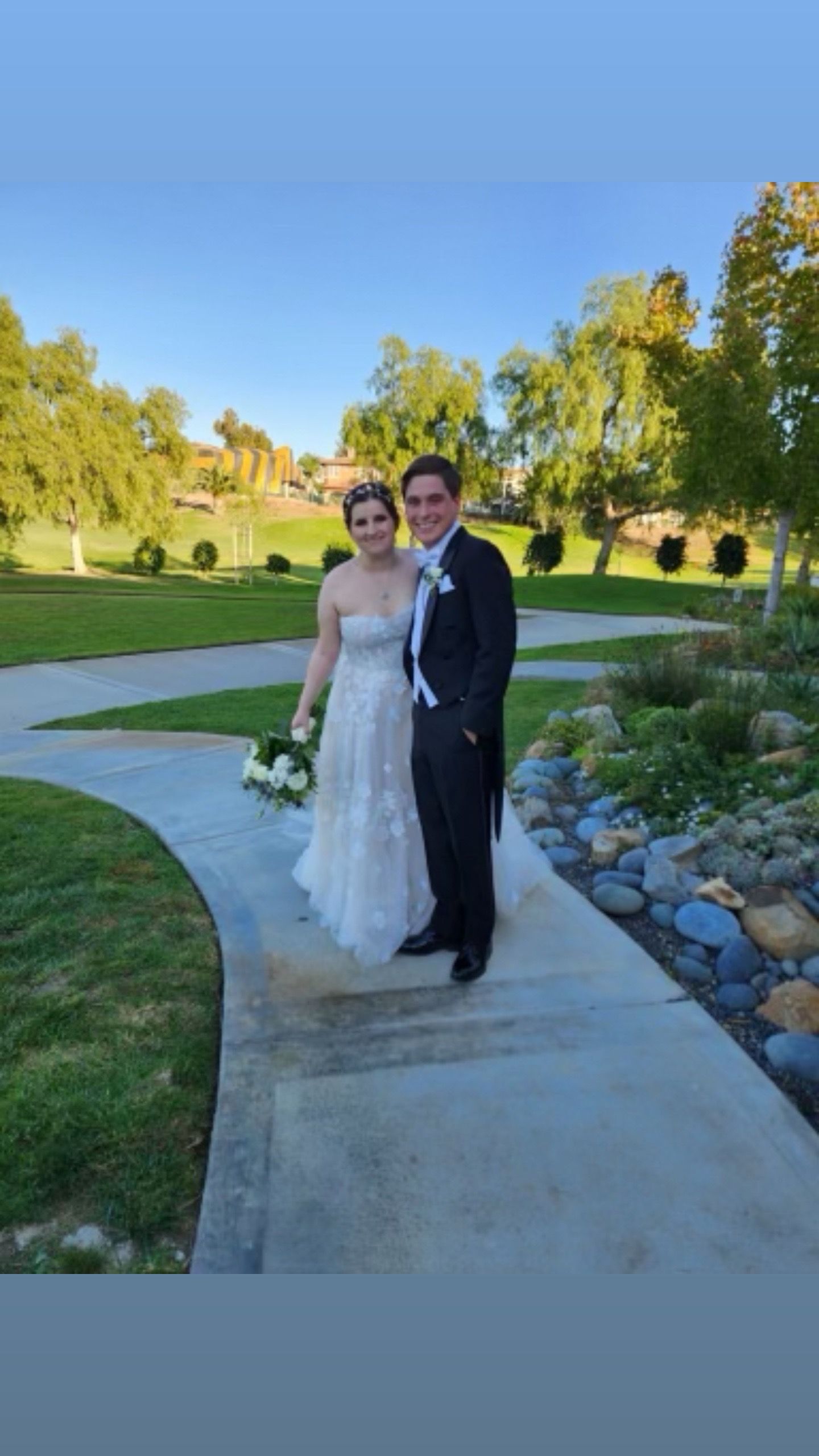 A bride and groom are standing next to each other on a sidewalk.
