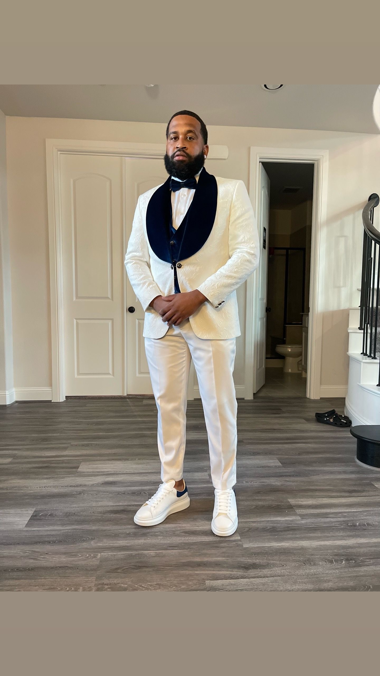 A man in a white tuxedo and white sneakers is standing in a room.