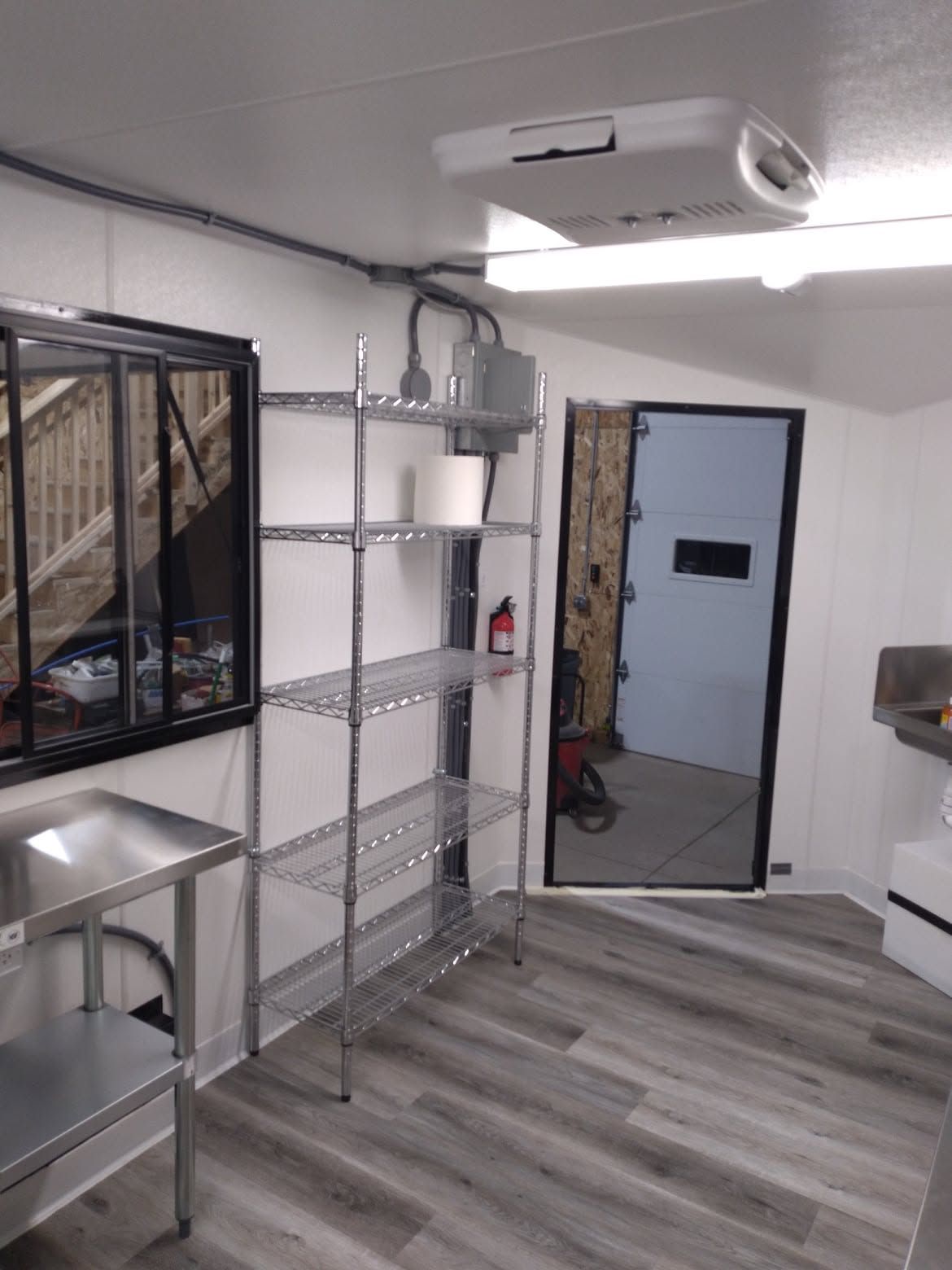 Small room with metal shelving, a sink, and an open door to a hallway, with gray wood-look flooring.