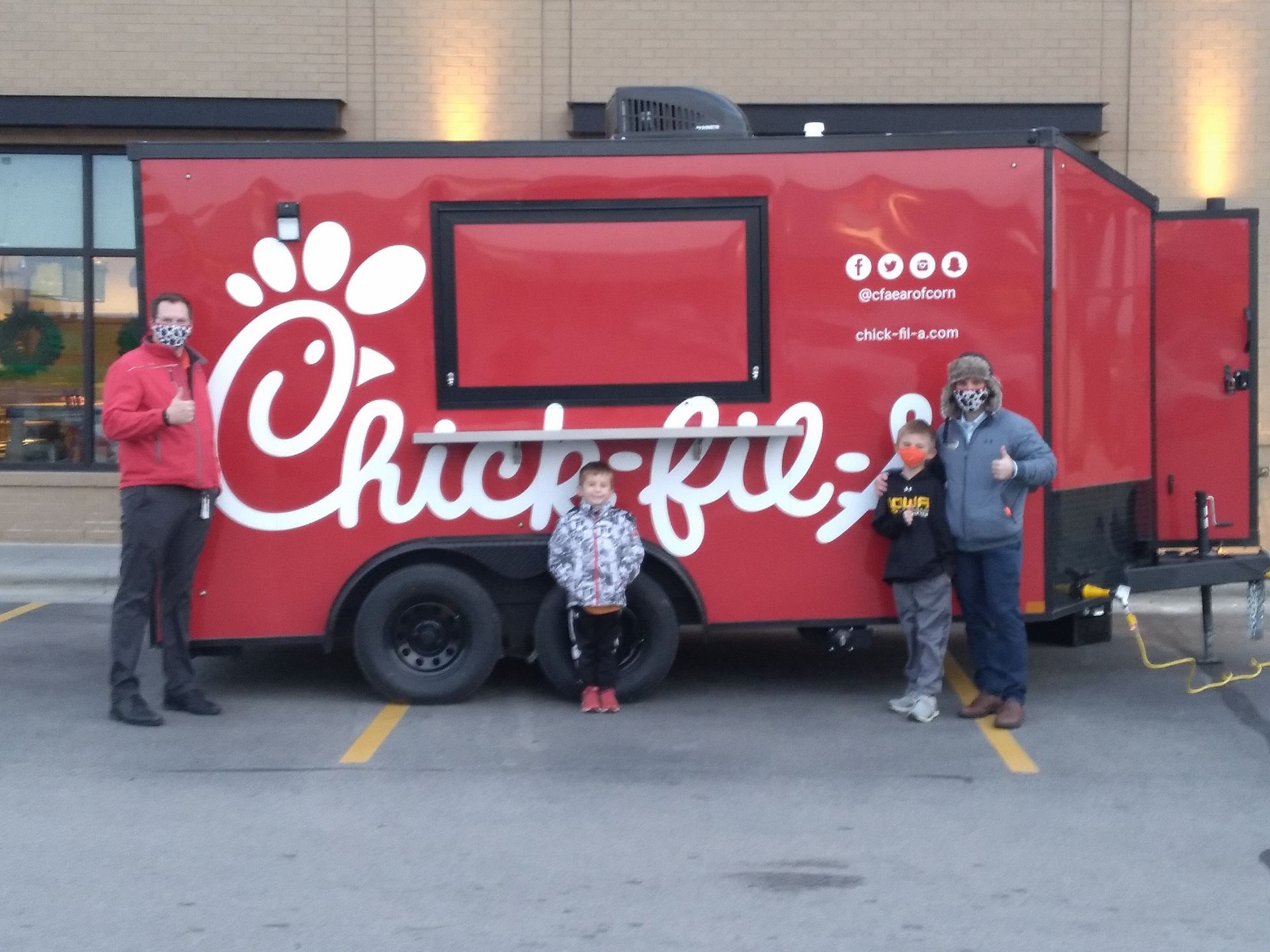 Red Chick-fil-A food truck with three people posing beside it in a parking lot