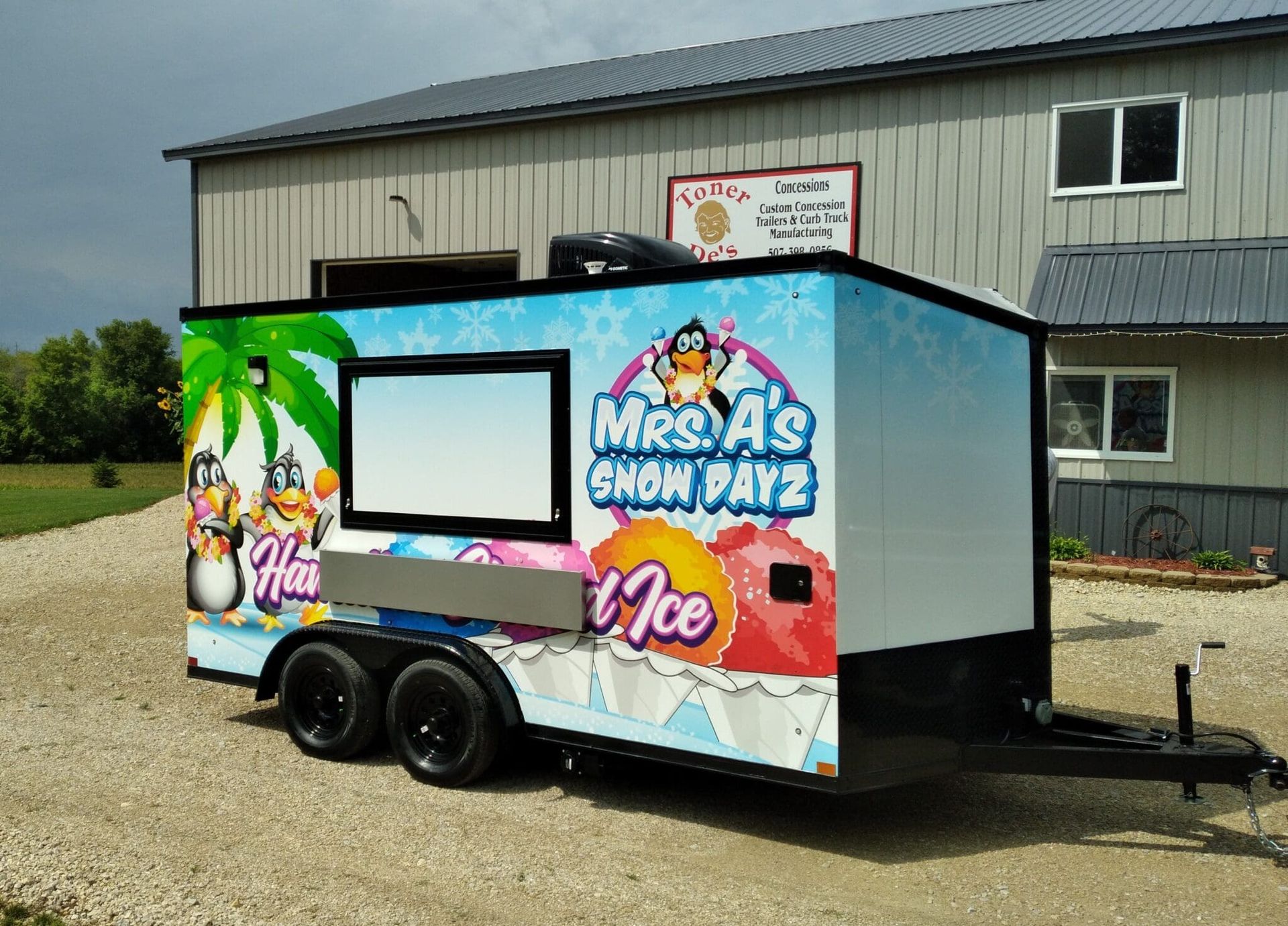 Colorful shaved ice trailer with palm tree graphics parked beside a warehouse