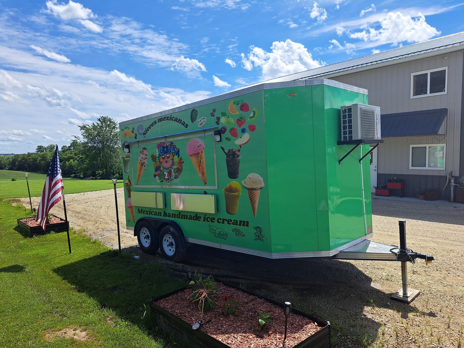 Bright green food trailer with mural art parked on grass beside a building under a blue sky.
