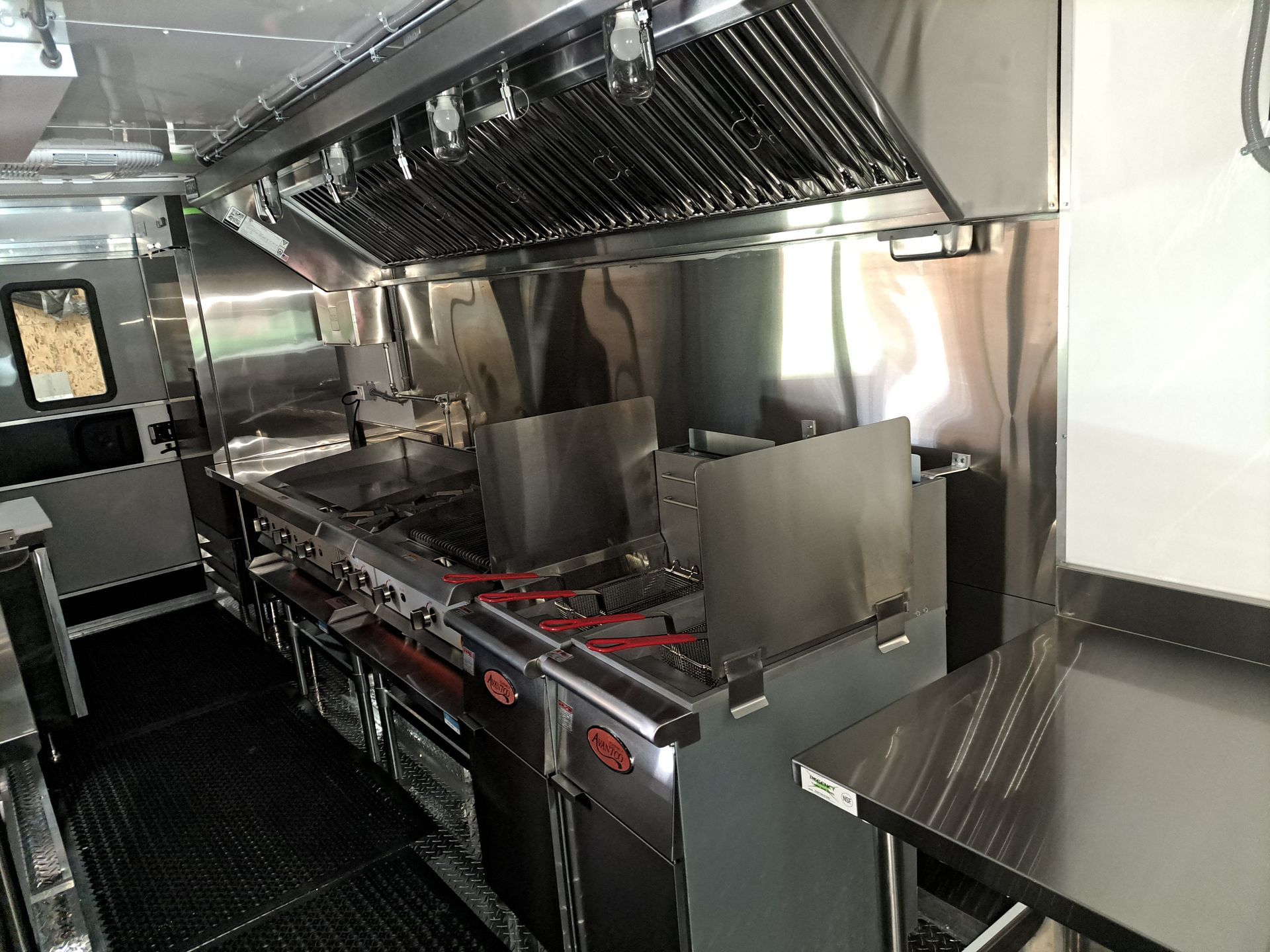 Commercial stainless steel kitchen with stove, ovens, and ventilation hood inside a narrow food truck-like space