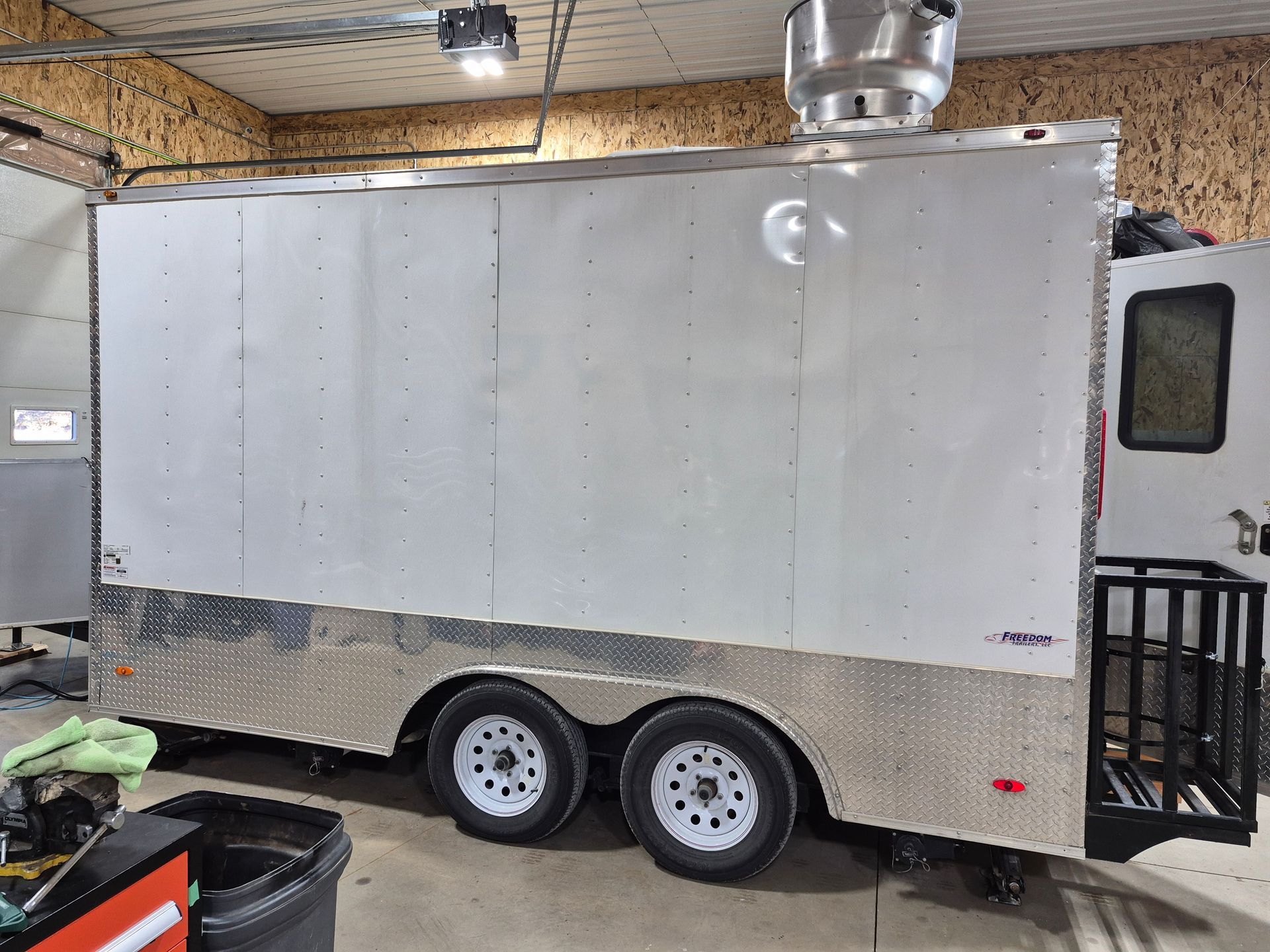 White enclosed cargo trailer in a workshop with a side door and dual wheels.