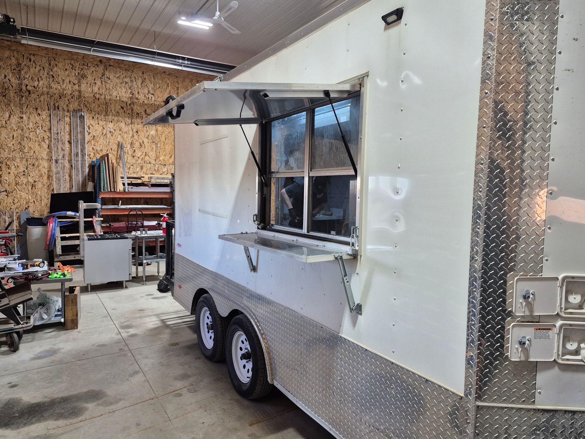 White food trailer under construction in a workshop, with silver diamond-plate trim and a service window.