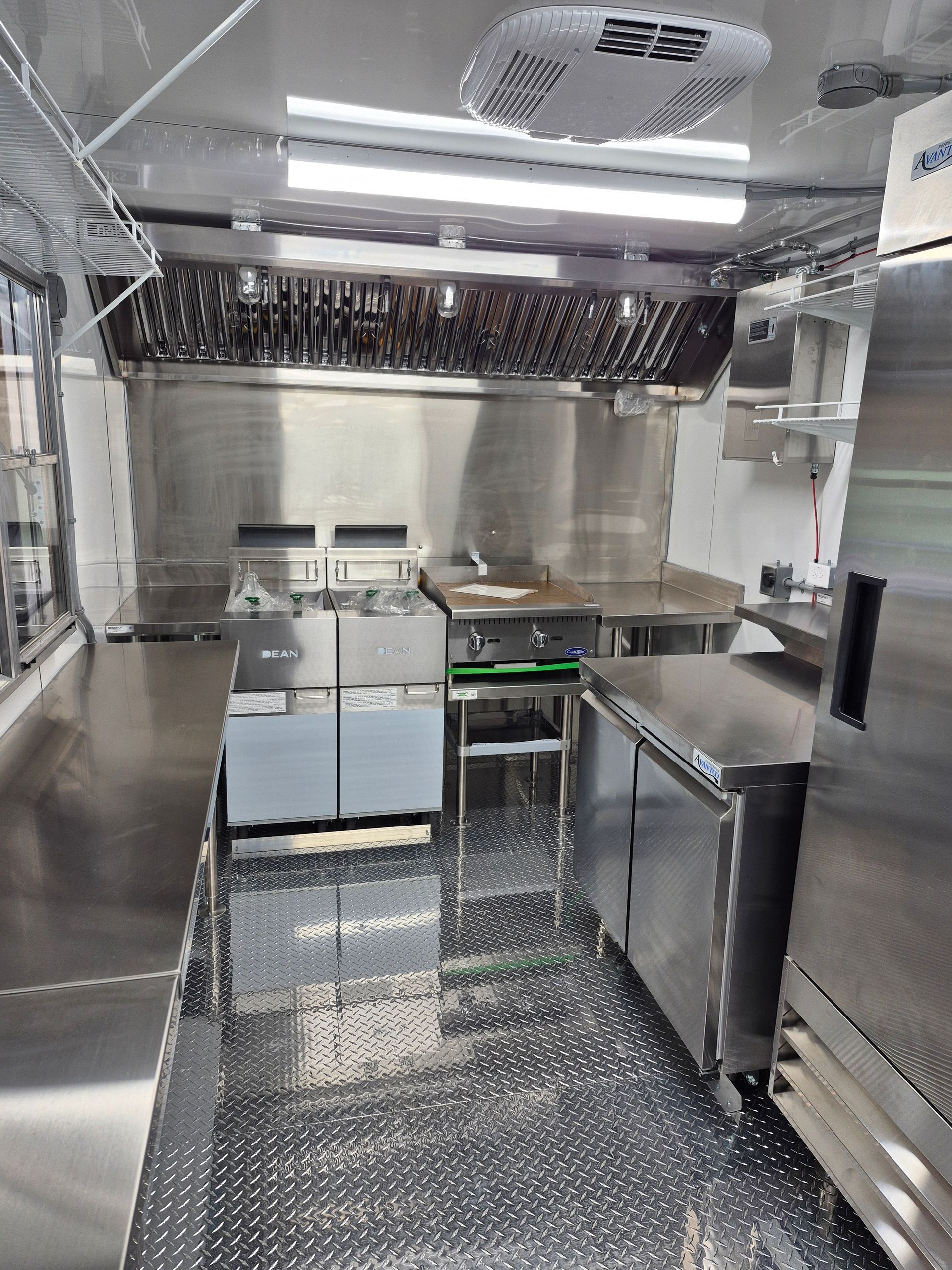 Stainless steel commercial kitchen with counters, oven, and sink on a diamond-pattern floor
