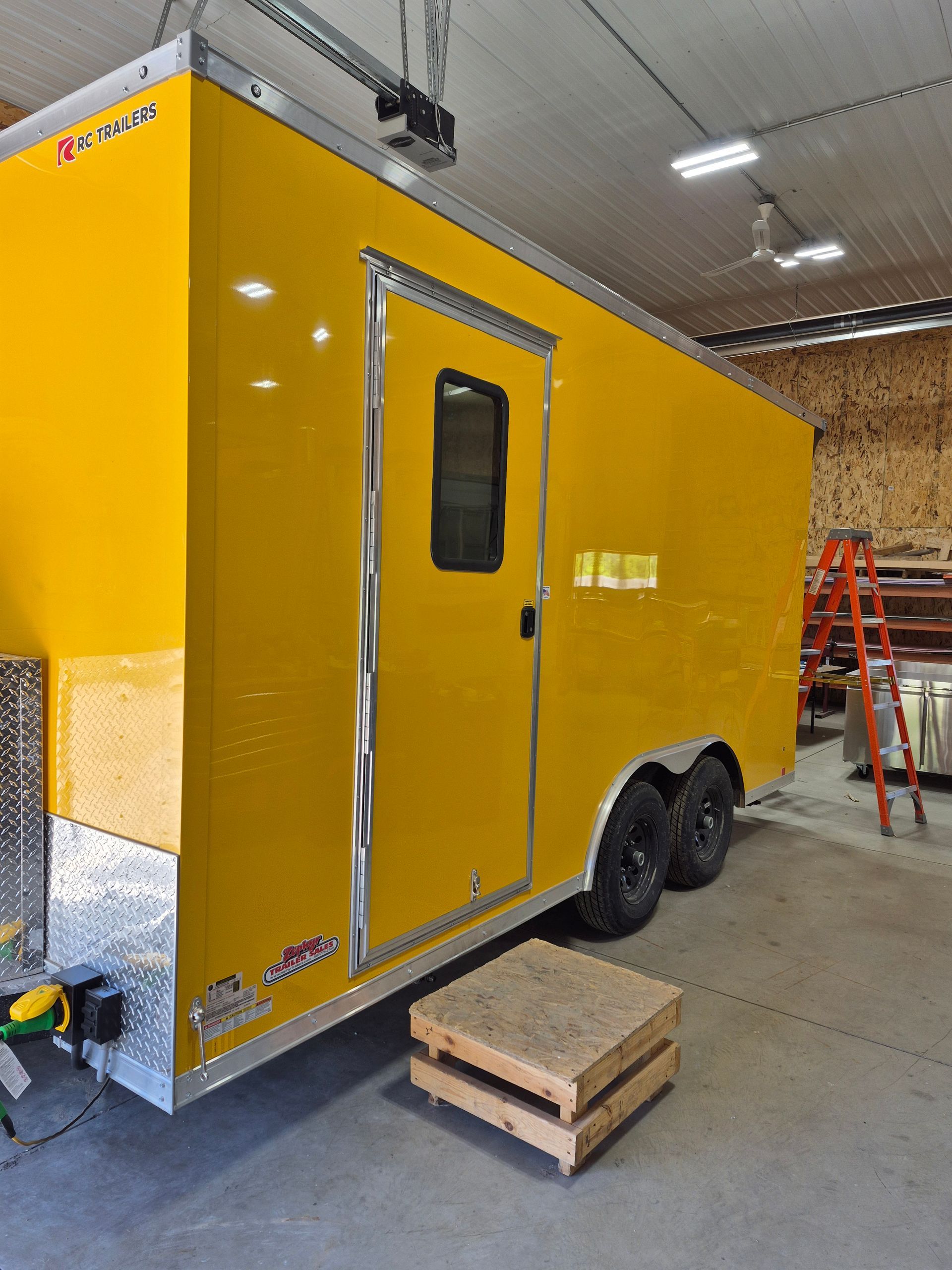 Yellow enclosed trailer in a garage, with a side door and two wheels visible.