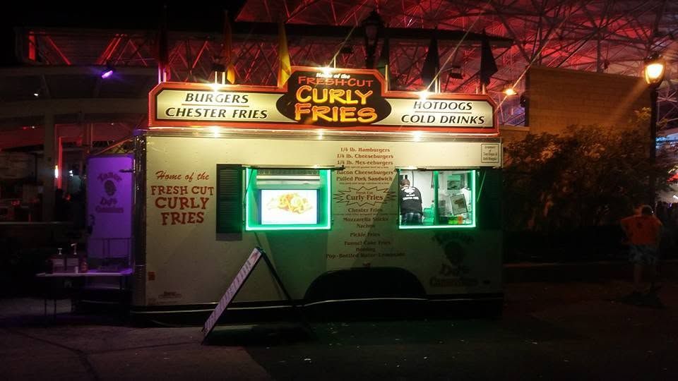 Small illuminated curly fries food stand at night with neon signs and red lights inside and around it