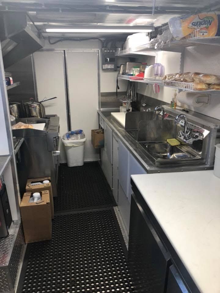 Narrow commercial kitchen with stainless counters, sink, shelves, and black rubber floor mats