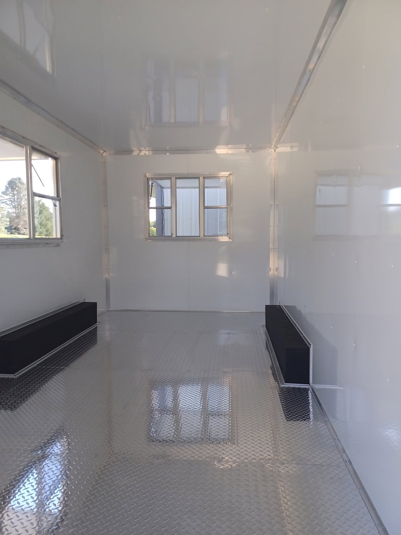 Empty white room with tiled floor, black benches along the walls, and several windows.