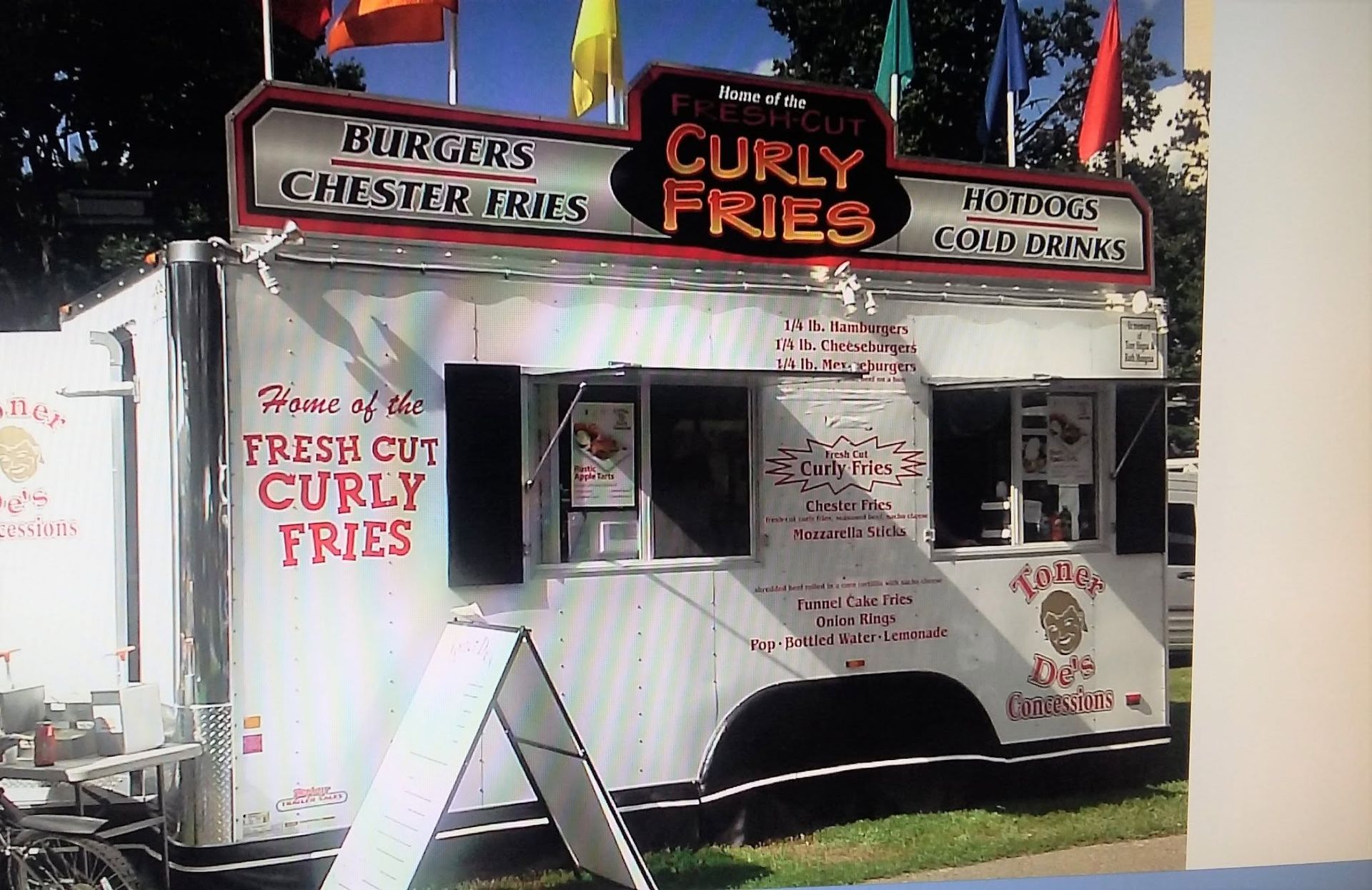Curly fries food truck with red-and-black signs parked outdoors under trees