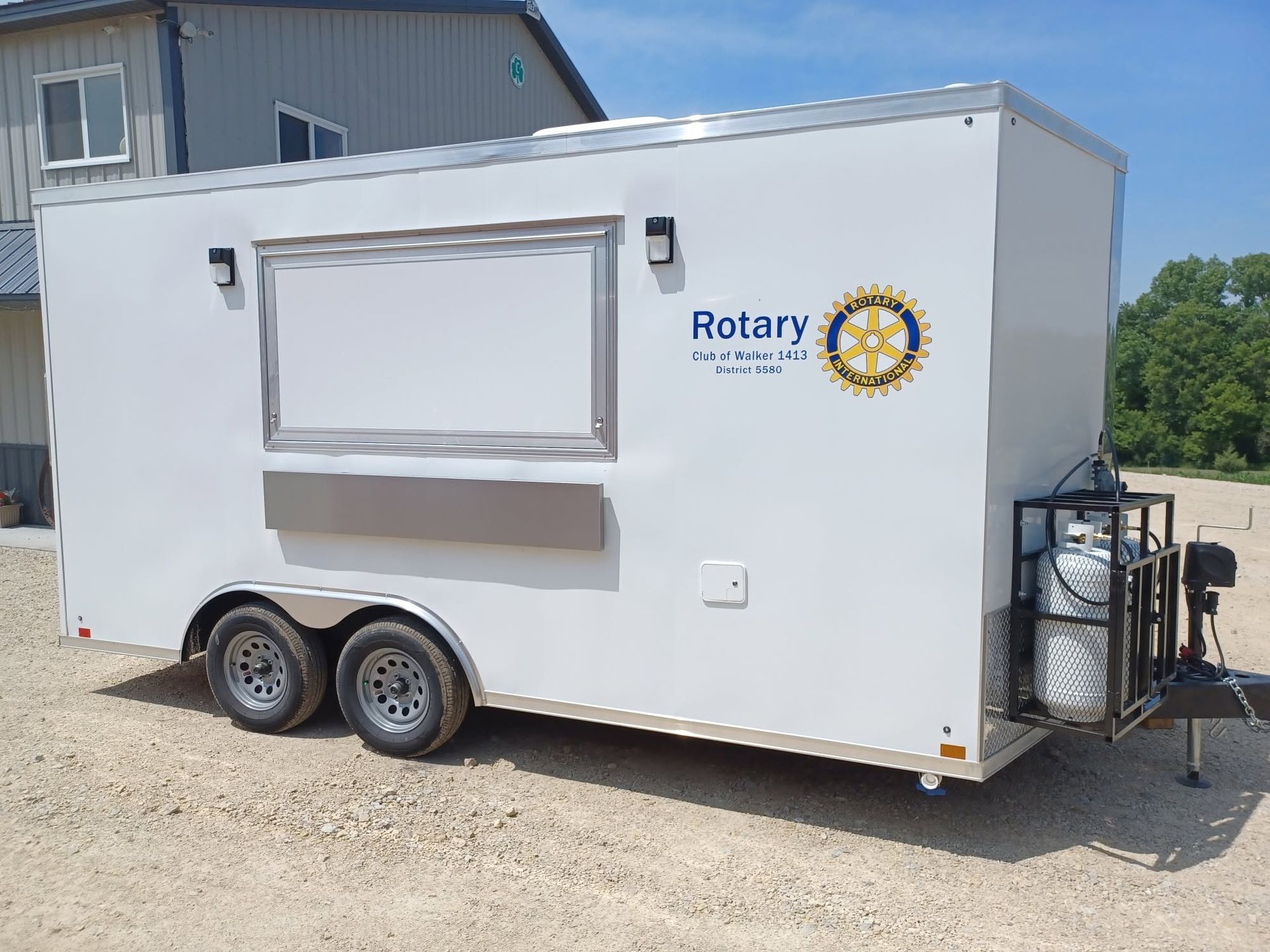 White Rotary concession trailer with serving window, dual wheels, and tanks parked on gravel outdoors