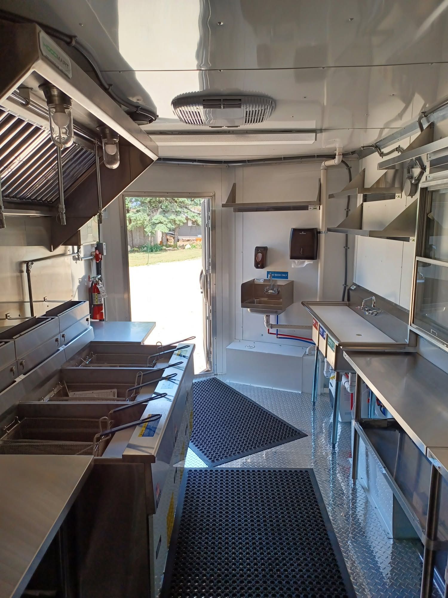 Interior of a food truck kitchen with stainless steel counters and open serving window at the back.