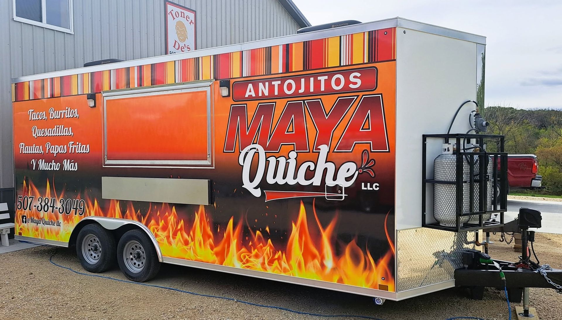 Food trailer with bright orange “Antojitos Maya Quiche” branding and flame graphics parked outdoors.
