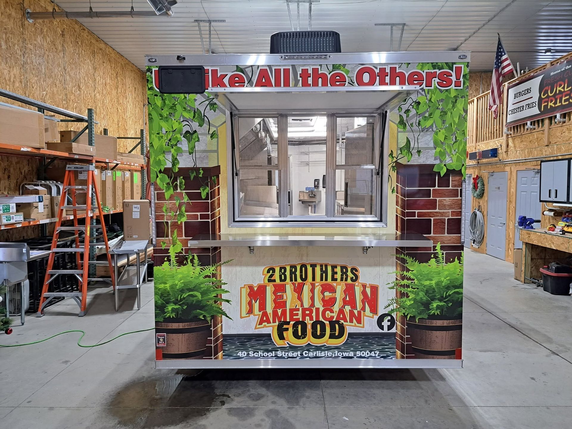 Food truck with large red sign and green plant graphics parked inside a warehouse.
