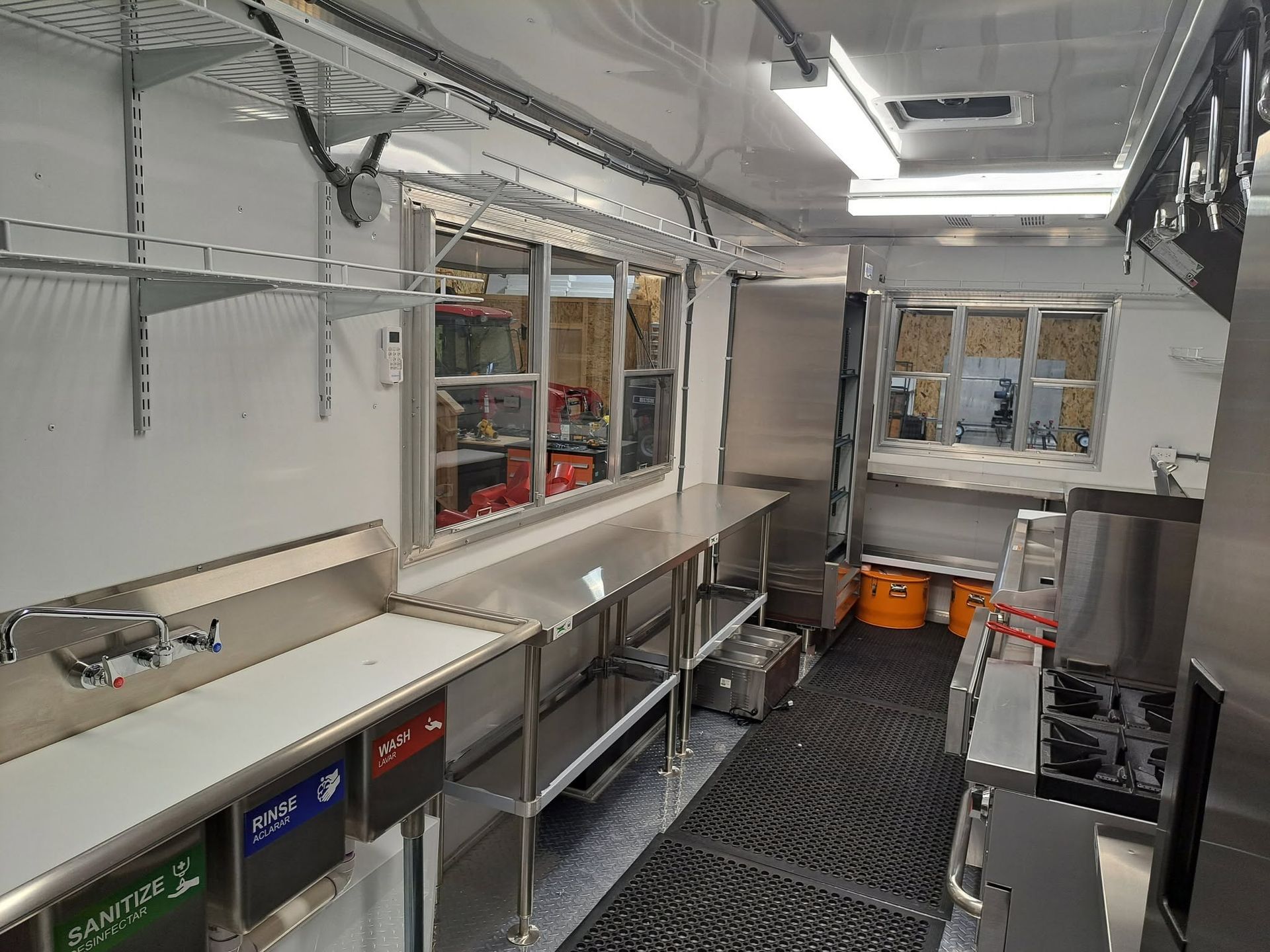 Compact mobile kitchen interior with stainless counters, shelves, and diamond-plate floor inside a truck trailer