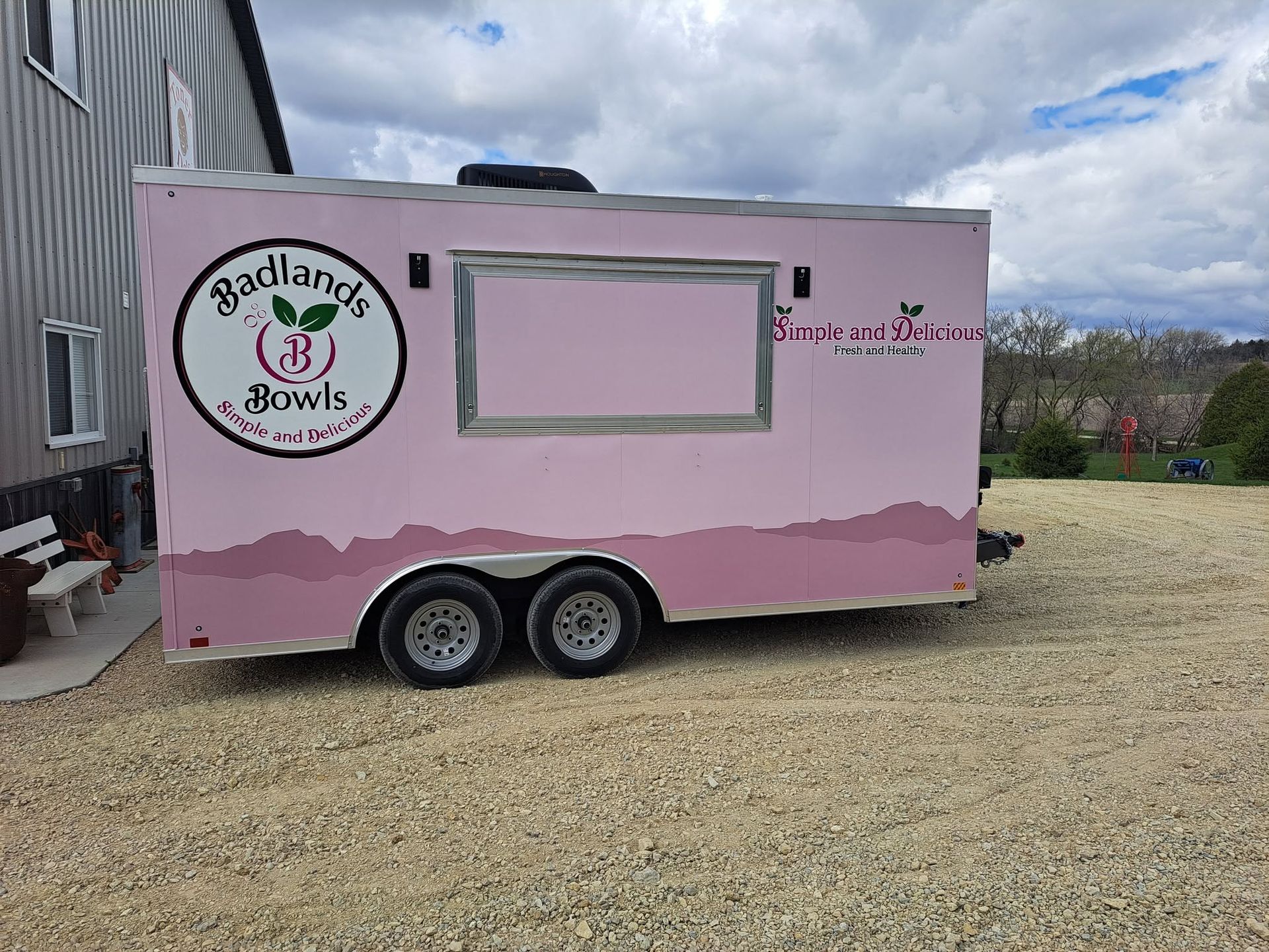 Pink food trailer with “Badlands Brownie” logo and serving window on gravel lot