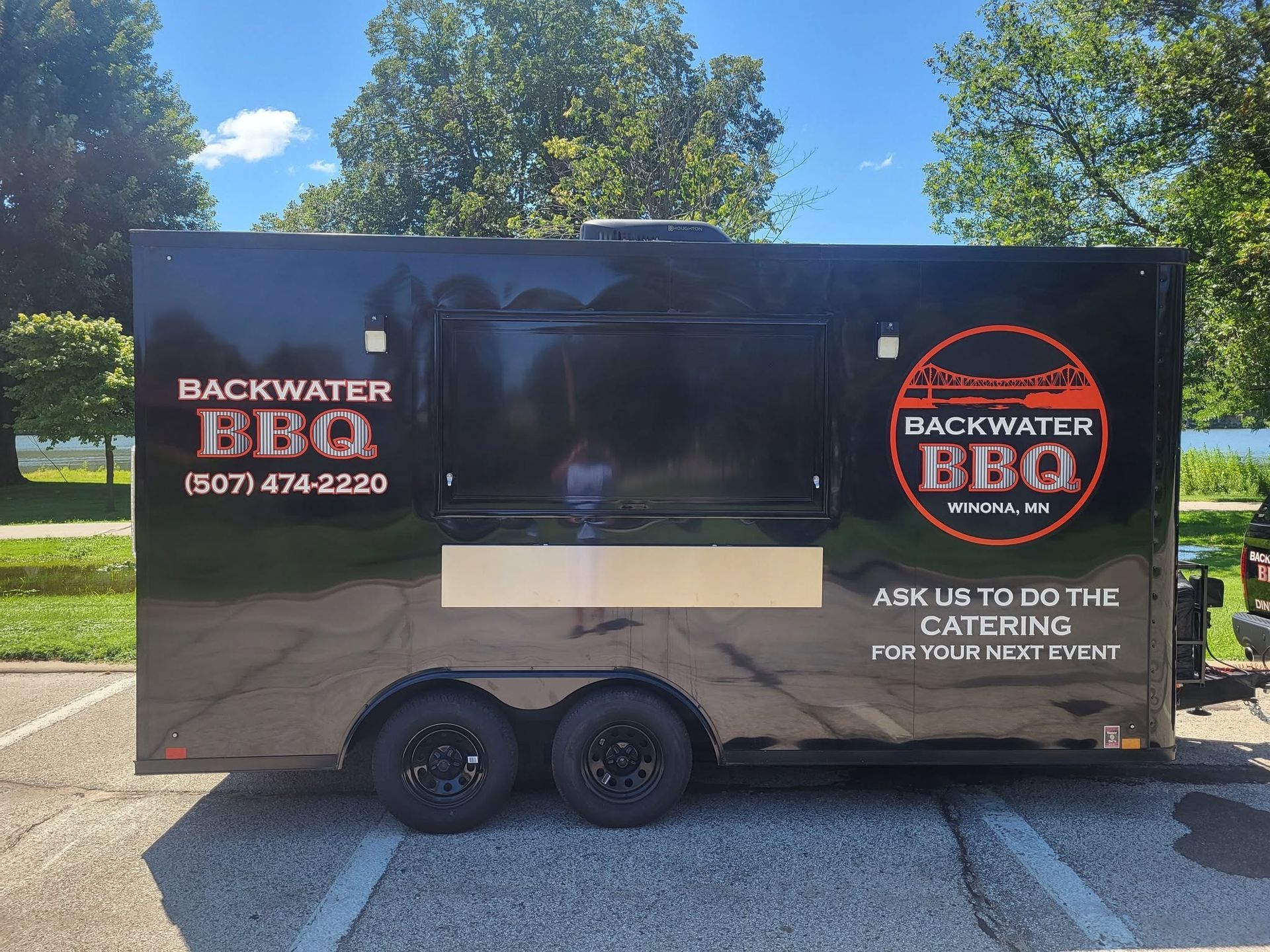 Black food trailer with Backwater BBQ logos parked in a sunny lot