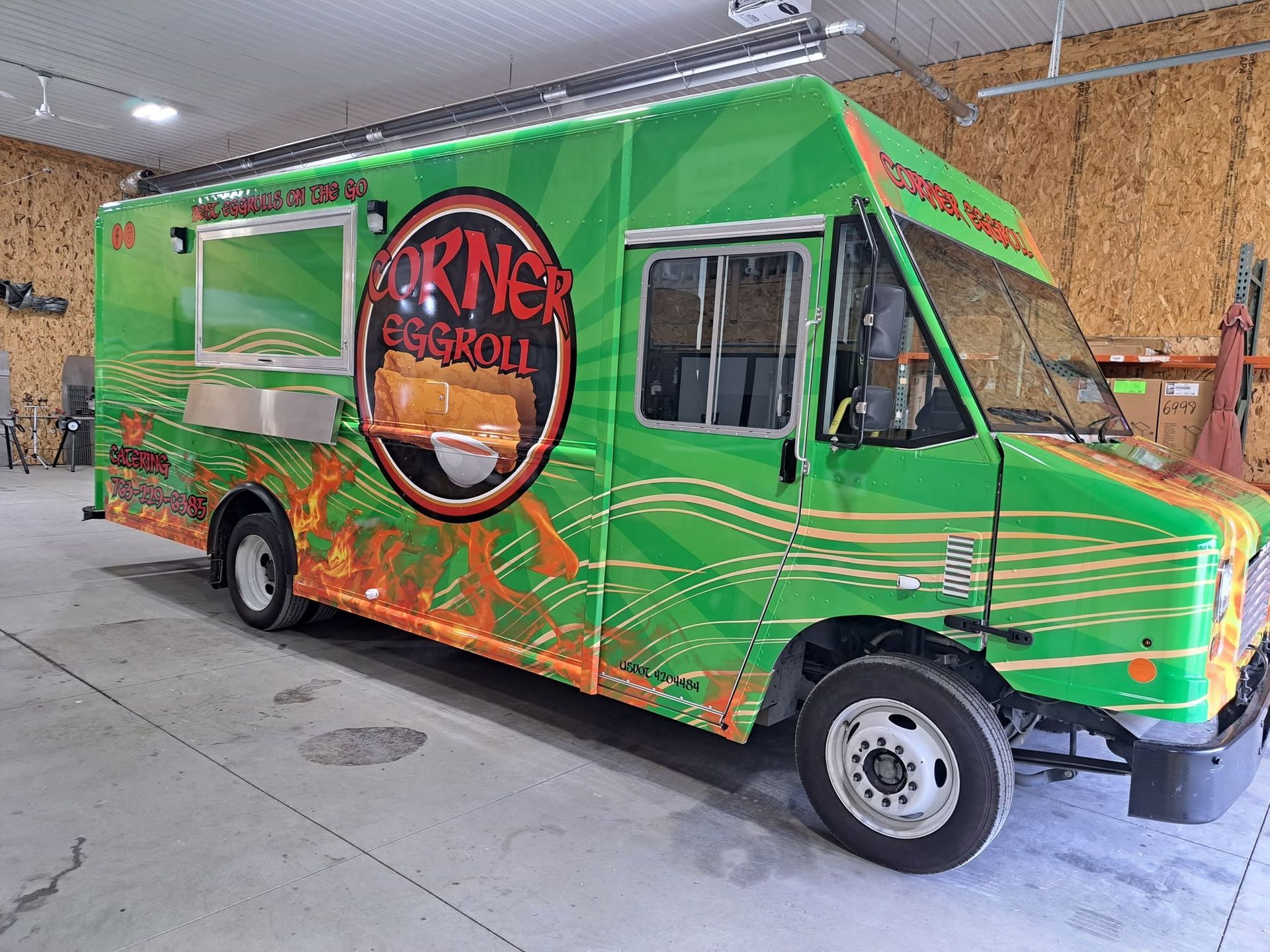 Green food truck with orange accents and a large circular logo parked indoors.