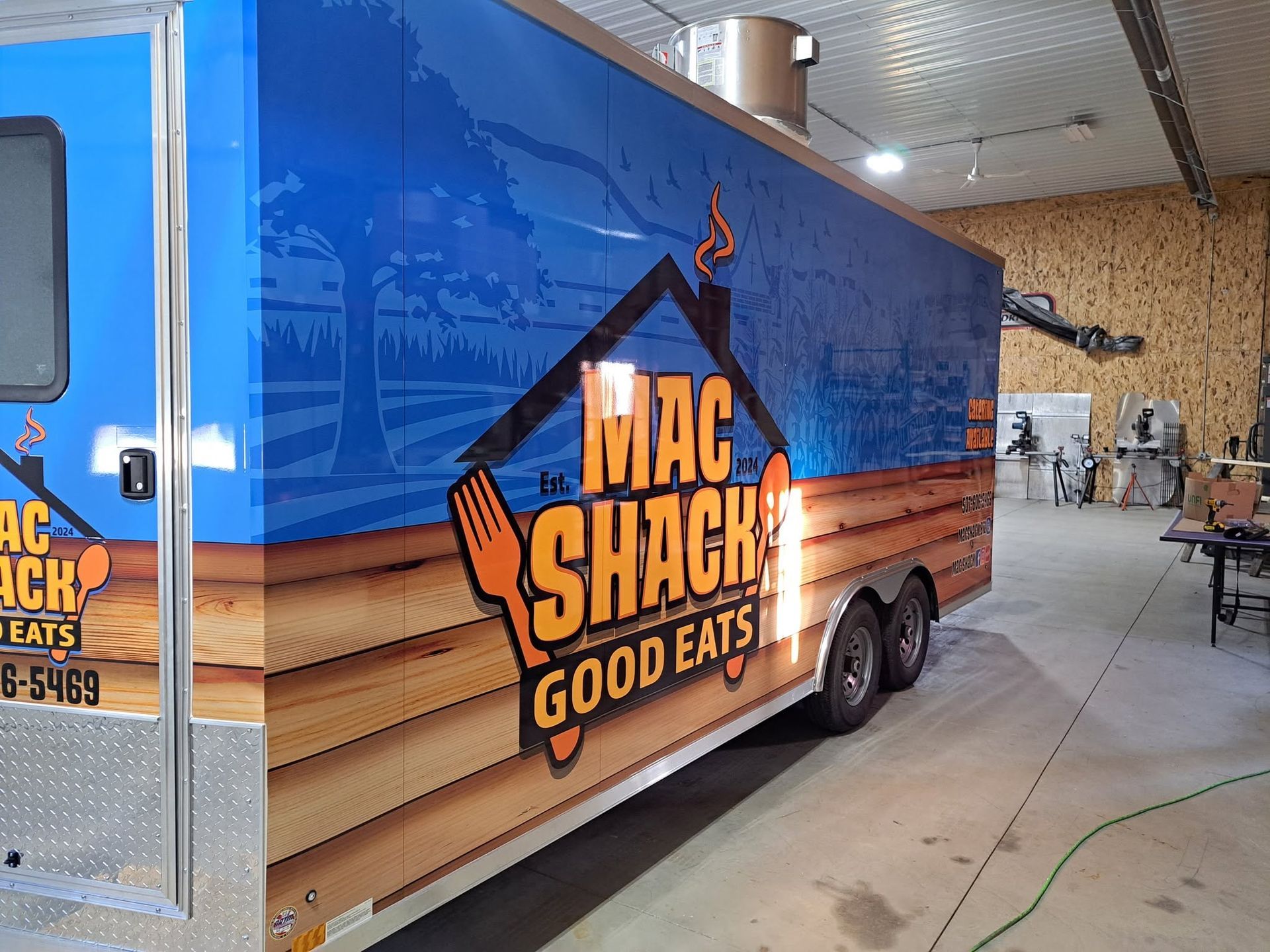 Blue Mac Shack food truck with orange logo parked indoors in a garage.