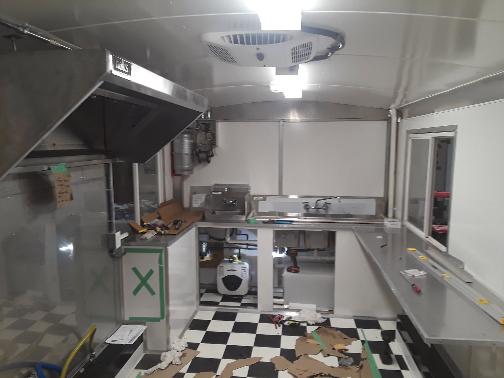 Small commercial kitchen with stainless counters, black-and-white floor, and scattered food debris on the floor