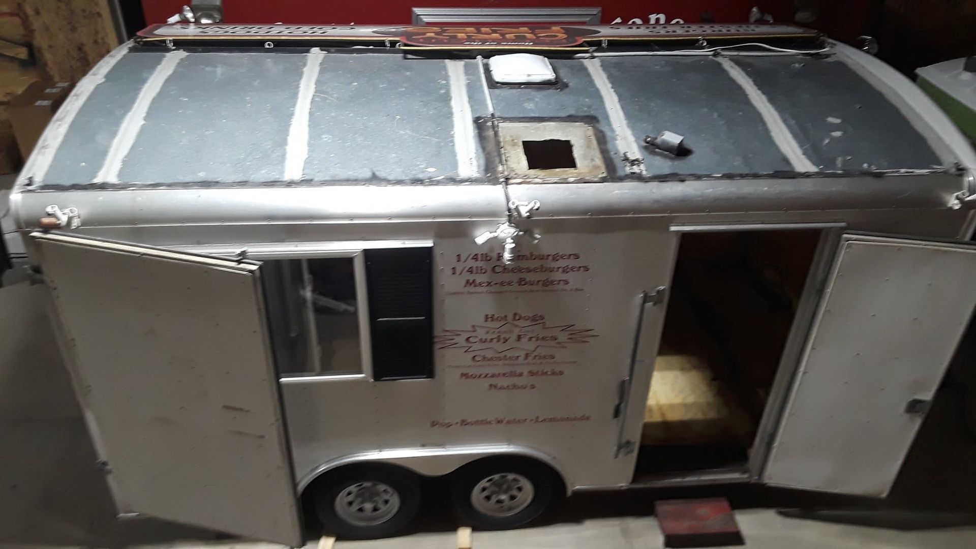 Silver trailer-style camper with two doors, small windows, and a rooftop ladder on a street.