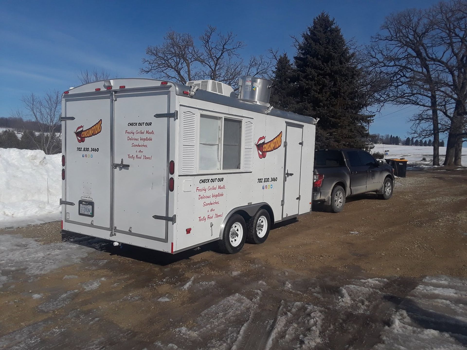 White dual-axle enclosed trailer hitched to a gray SUV in a snowy yard under a blue sky.