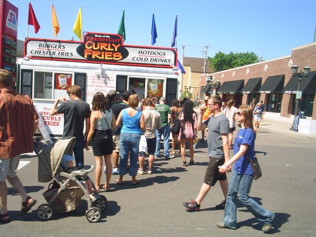 Crowded fairground food stand with people waiting in line under colorful flags on a sunny day