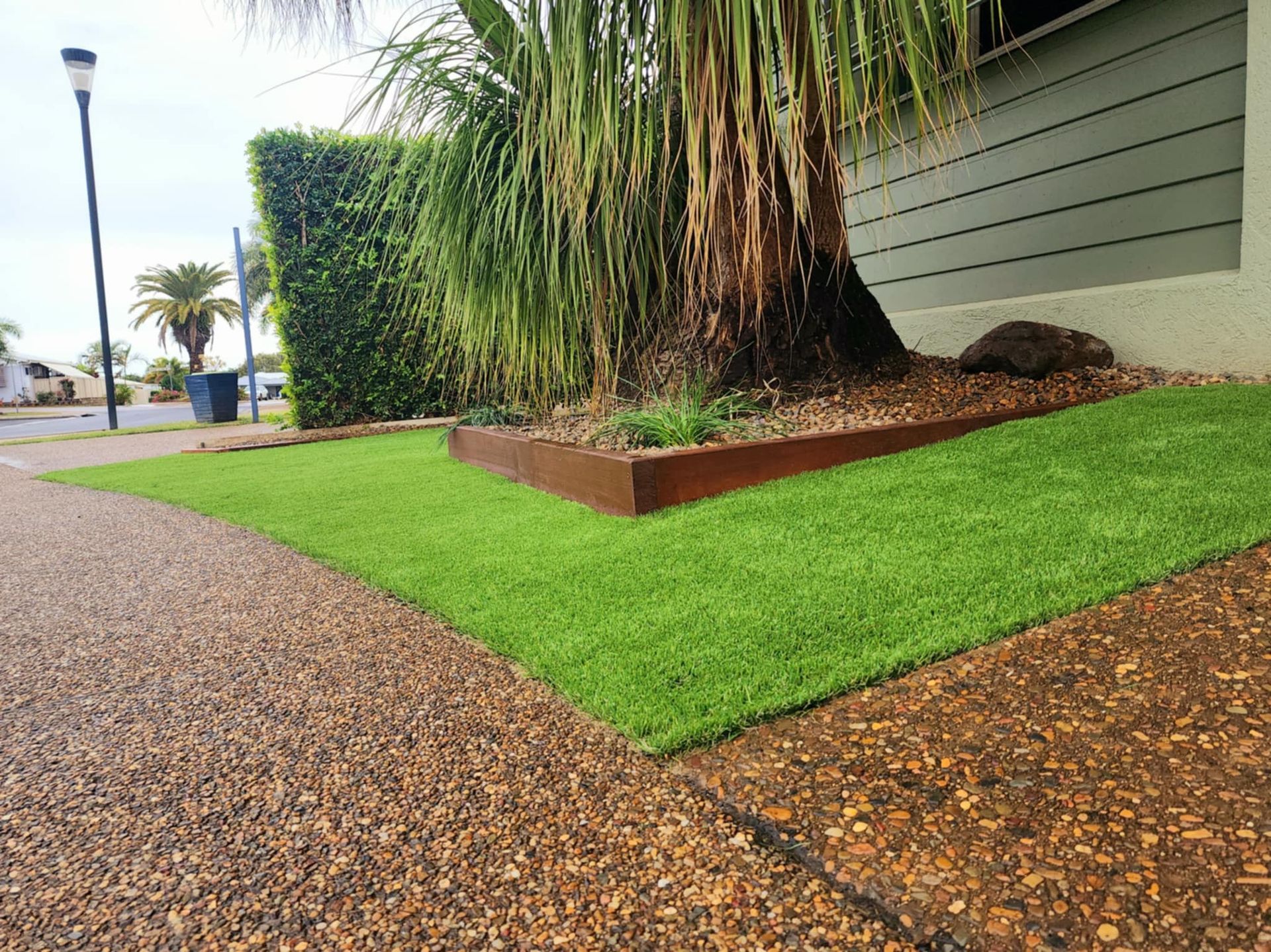 Green Lawn With a Brown Border Next to a Textured Sidewalk and a Palm Tree — On The Mark Landscaping in Branyan, QLD
