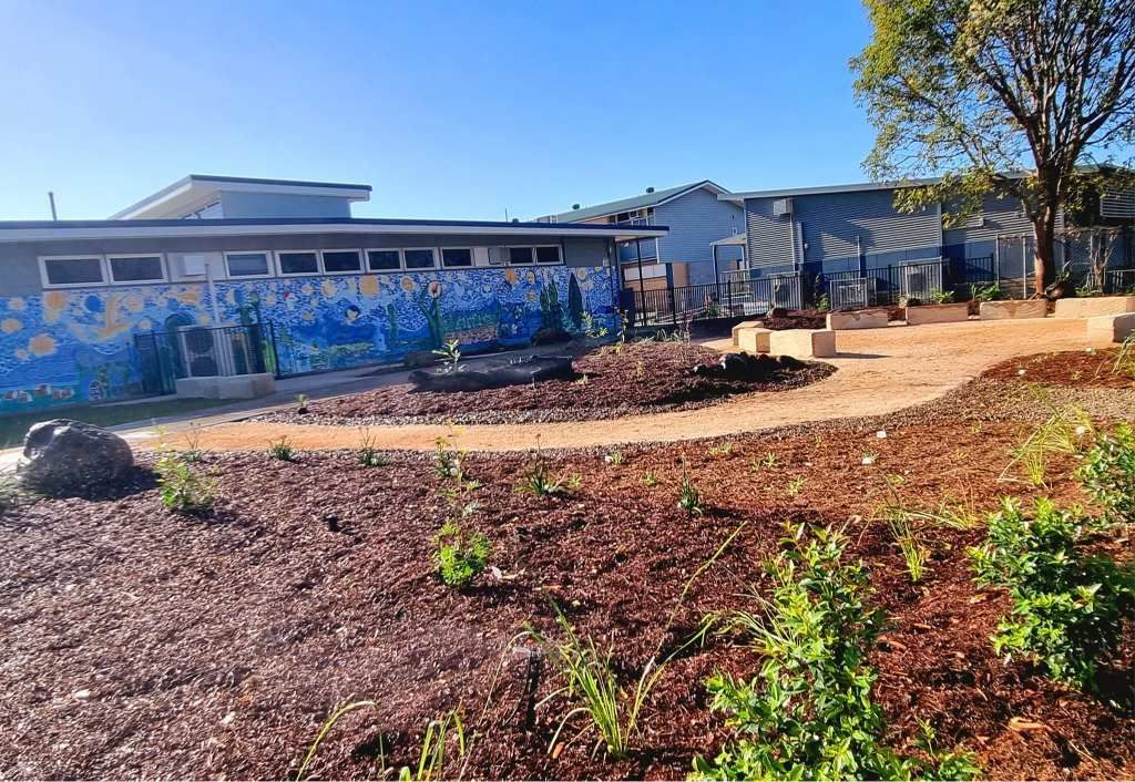 A School Building With a Blue Mural, Brown Mulch, and a Gravel Pathway — On The Mark Landscaping in Branyan, QLD