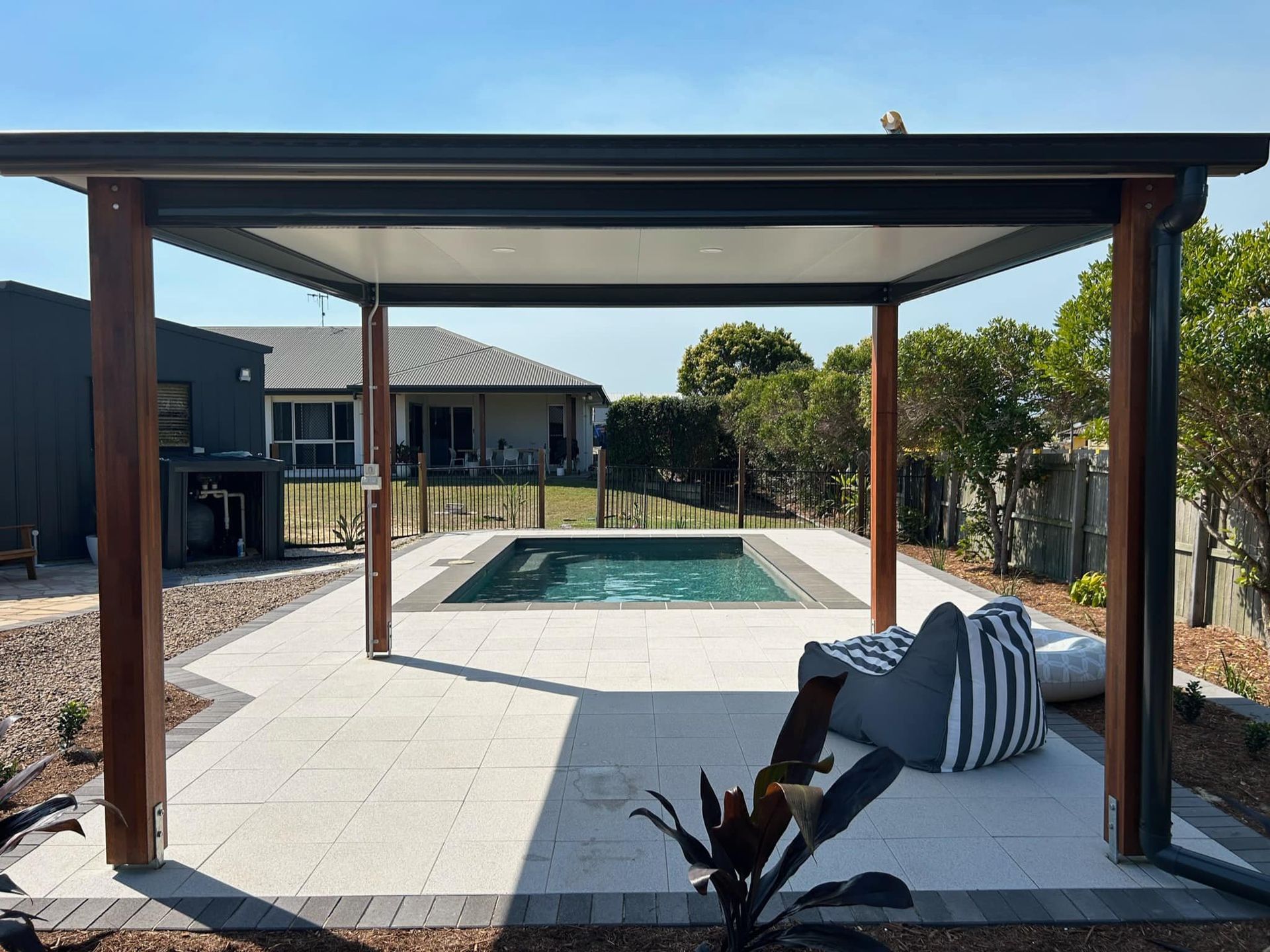 Patio With Dark Pergola, Pool, and Seating; Sunny Outdoor Setting — On The Mark Landscaping in Branyan, QLD