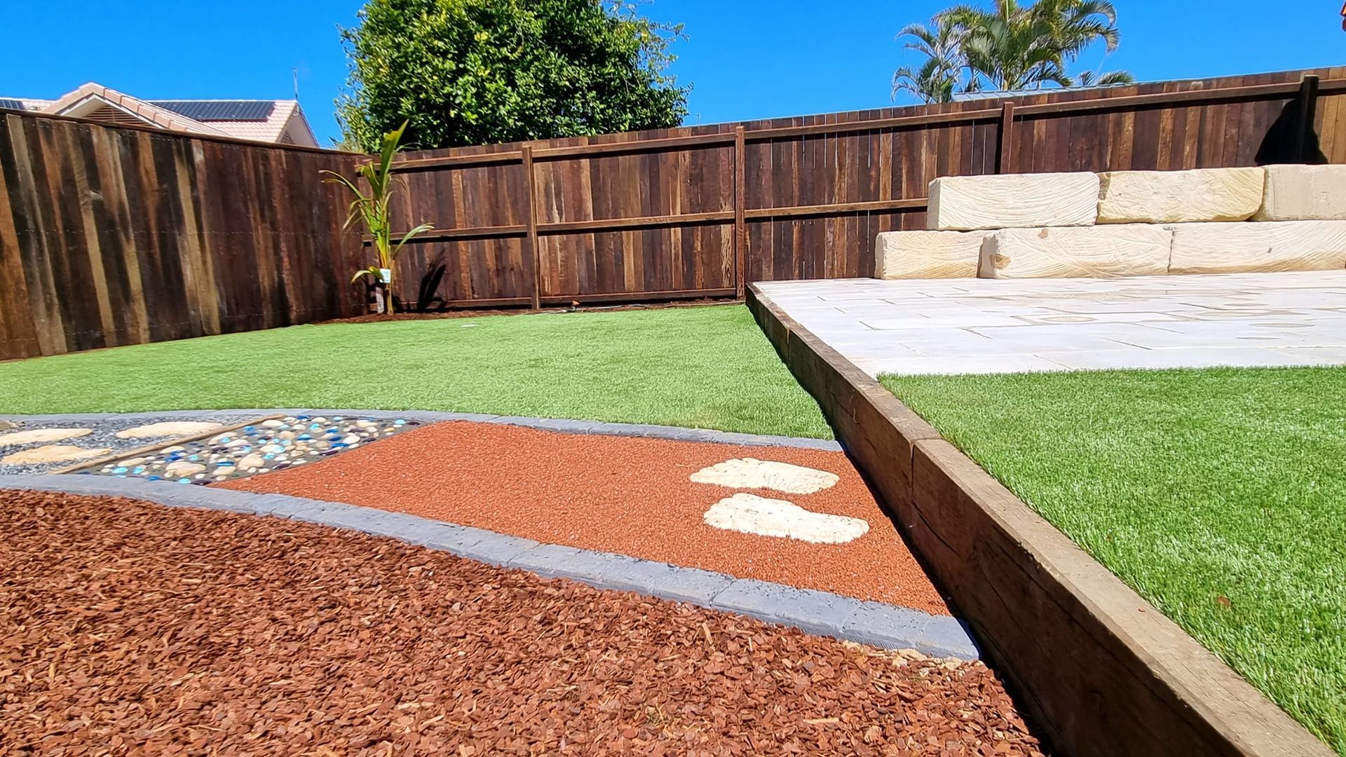 Backyard With Wood Fence, Lawn, Stone Steps, a Pebble Path, and Wood Chip Bed — On The Mark Landscaping in Branyan, QLD
