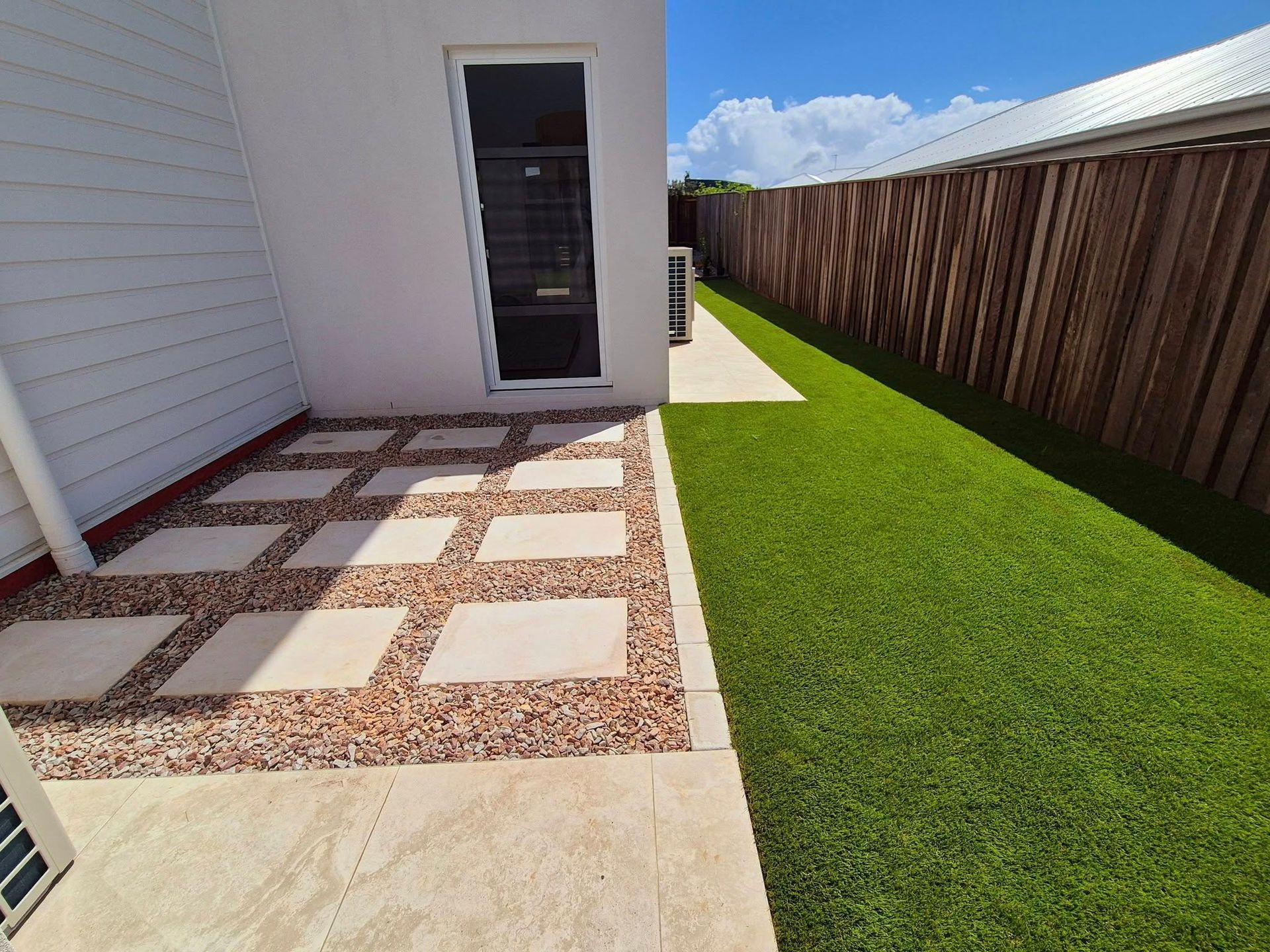 Patio With Stone Pavers and Gravel, Next to Artificial Lawn and a Wooden Fence — On The Mark Landscaping in Branyan, QLD