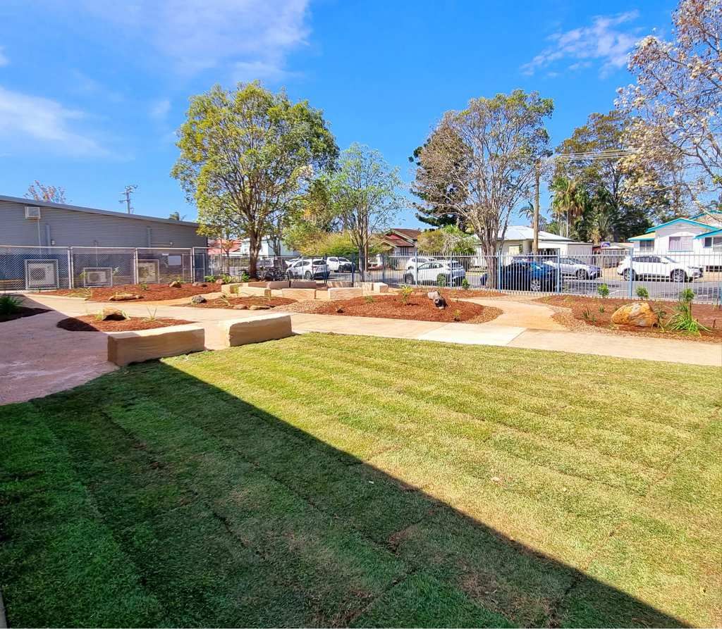 Lawn and Garden Beds in an Outdoor Space With Trees, Buildings, and a Blue Sky — On The Mark Landscaping in Branyan, QLD