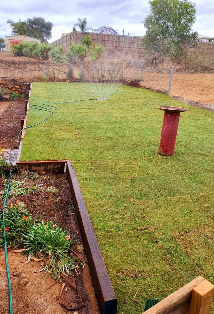 Green Lawn in Backyard With Sprinkler, Red Post, and Raised Garden Bed — On The Mark Landscaping in Branyan, QLD