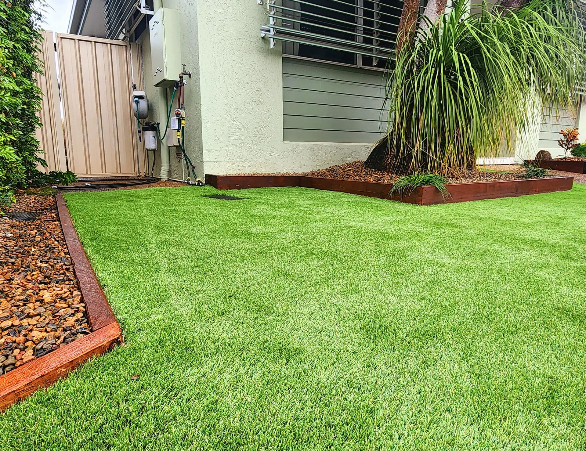 Green Artificial Lawn With Brown Border Edging a Building and a Gate — On The Mark Landscaping in Branyan, QLD