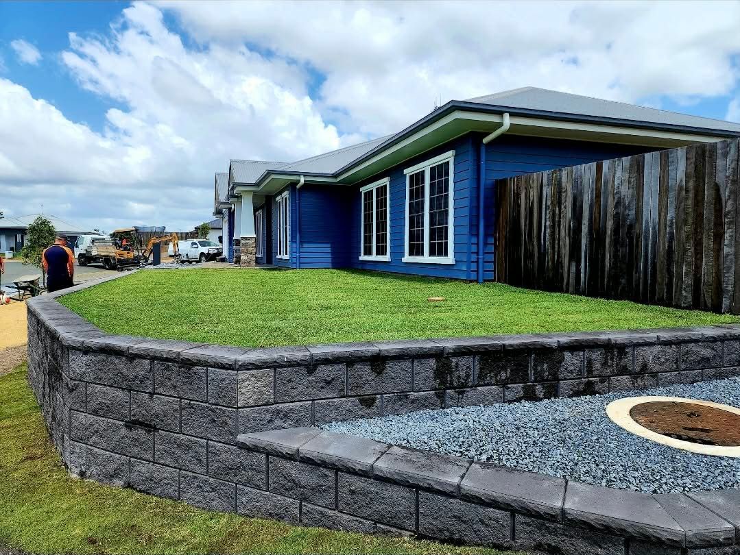 Blue House With Retaining Wall and Grassy Lawn Under a Partly Cloudy Sky — On The Mark Landscaping in Branyan, QLD