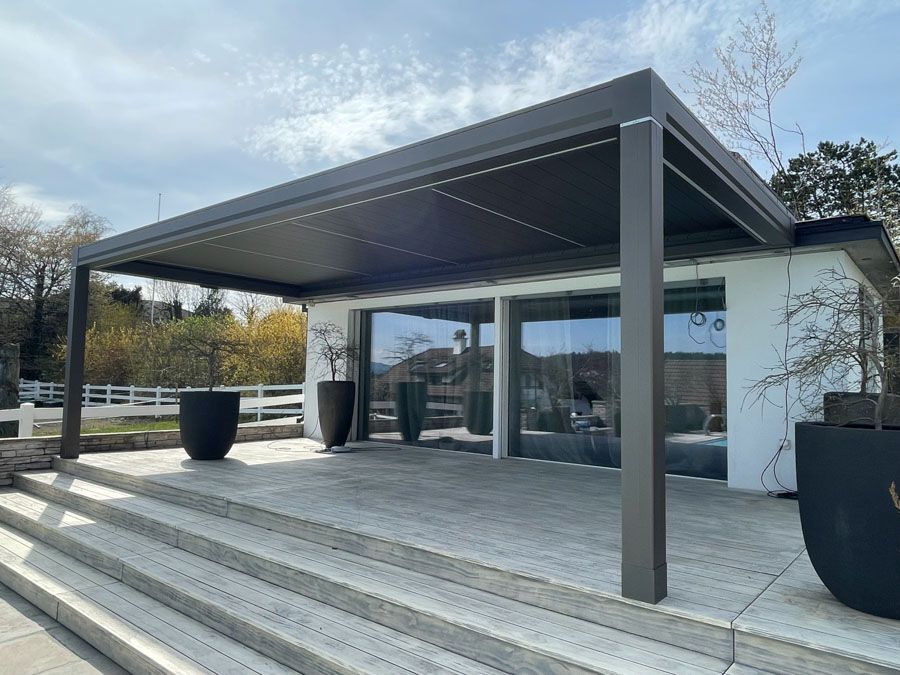 Eine Pergola steht auf einer Terrasse neben einem Gebäude.