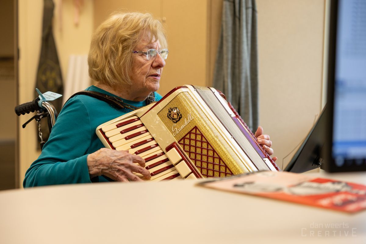 An elderly woman in a wheelchair is playing an accordion.