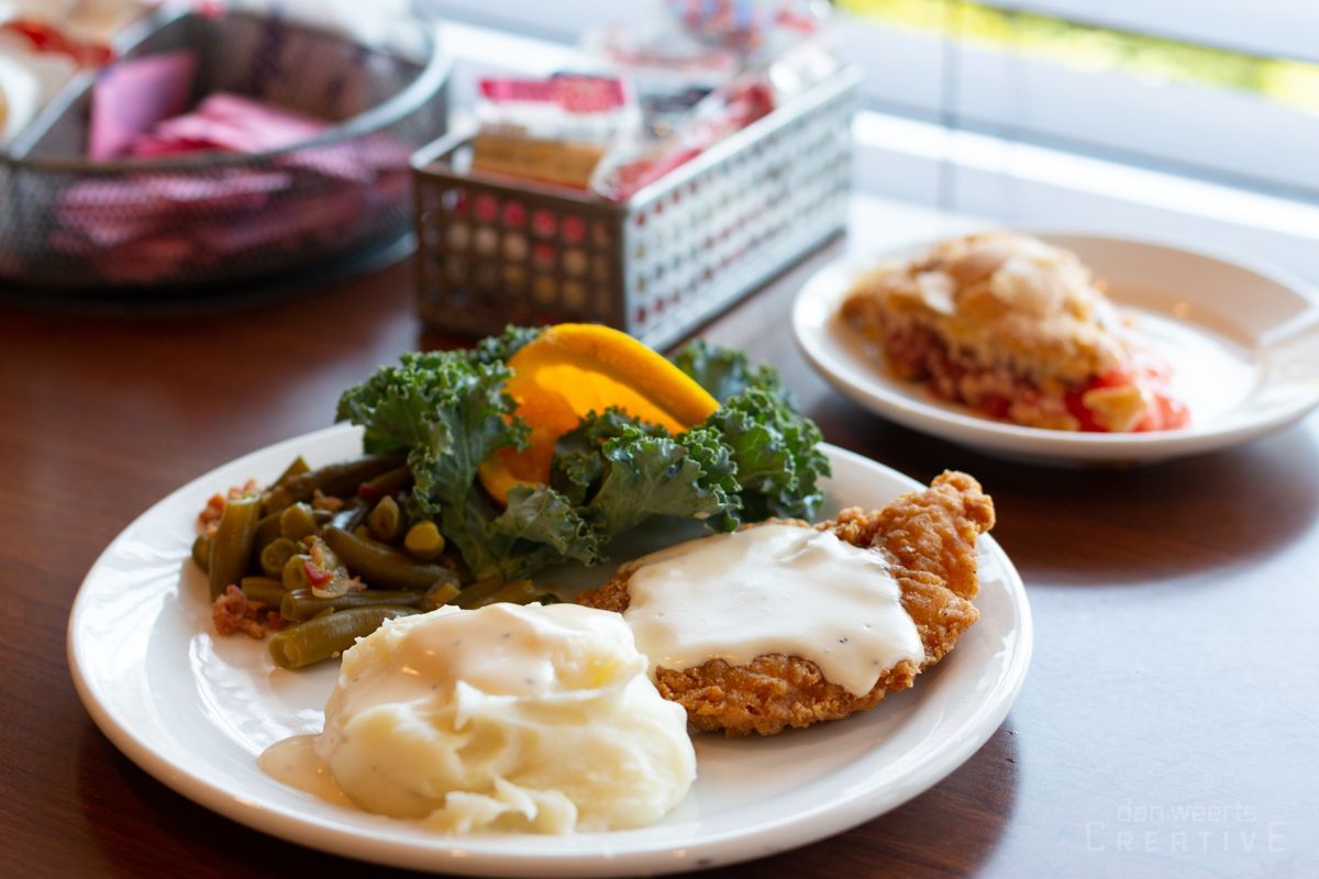 A plate of food with chicken , green beans , mashed potatoes and gravy on a table.