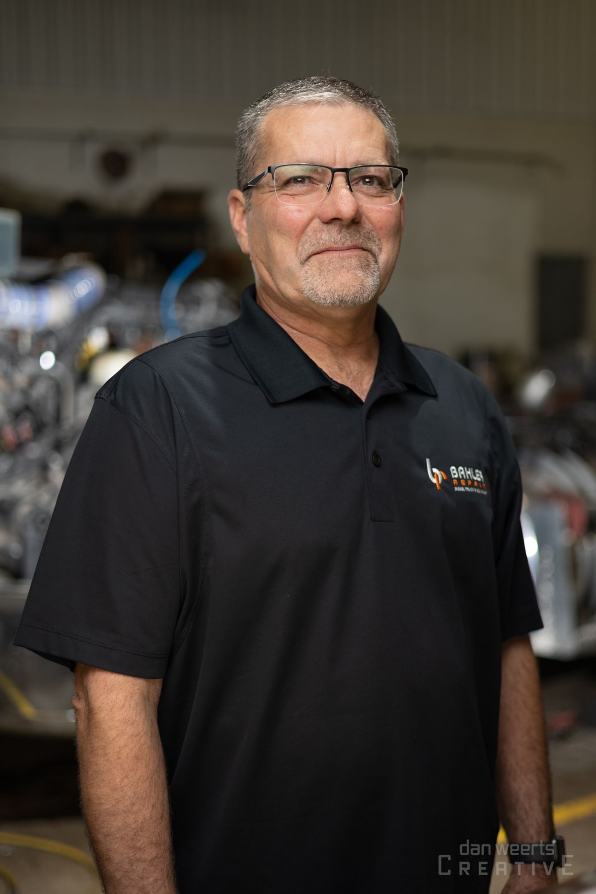 A man wearing glasses and a black shirt is standing in a garage.
