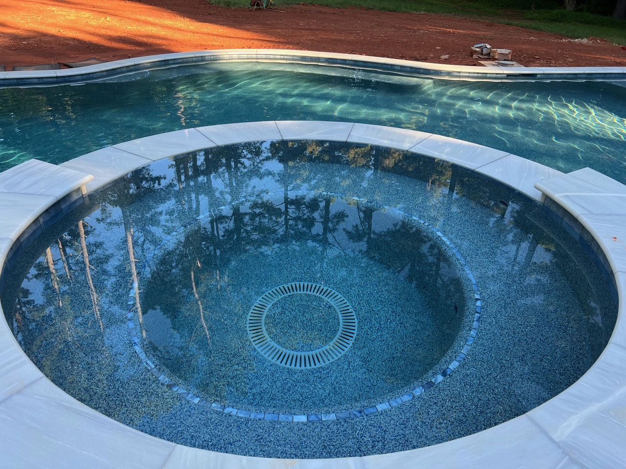 A swimming pool with a circular hot tub in the middle of it.