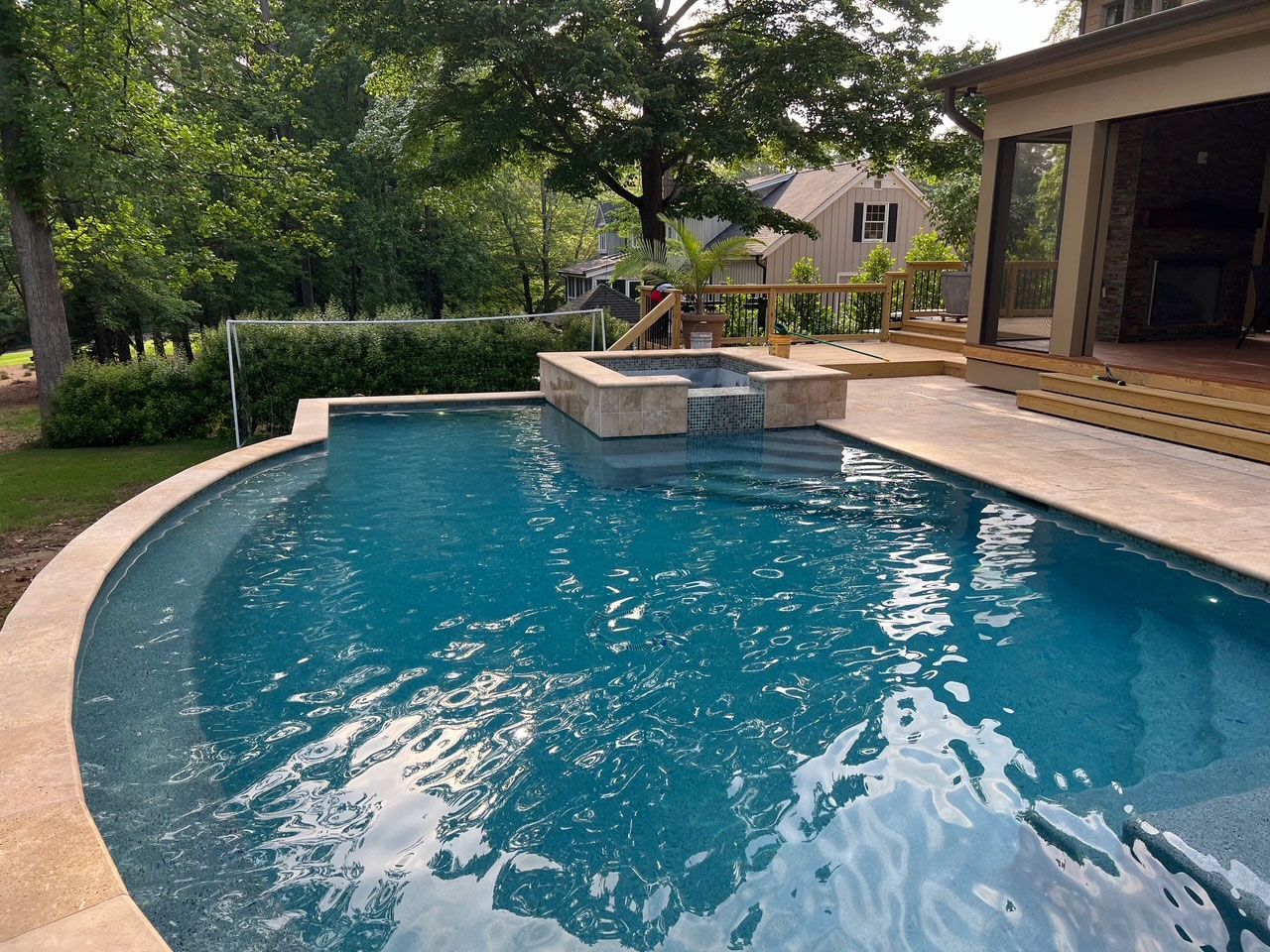 A large swimming pool is surrounded by trees and a house