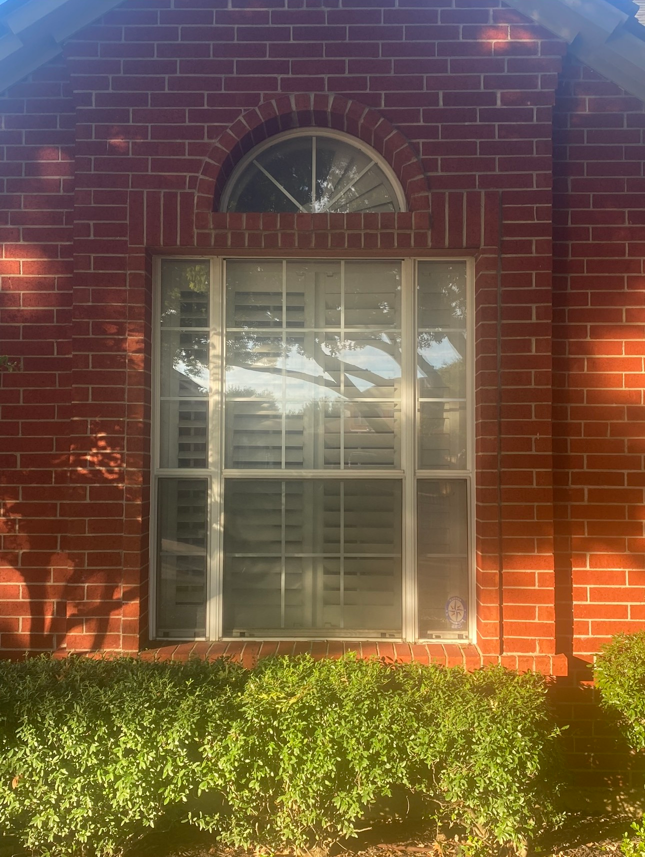 A red brick house with a large window and shutters.
