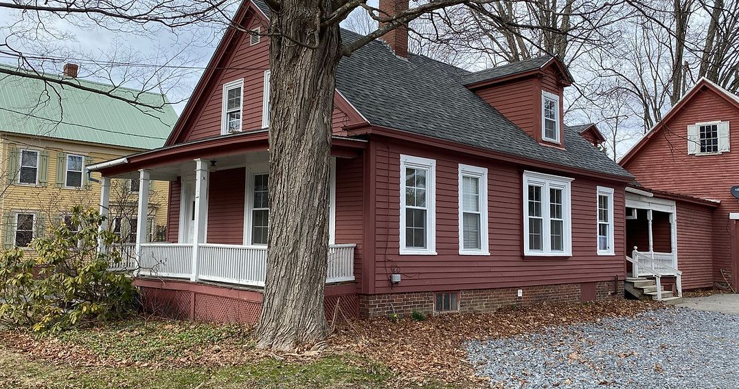 A red house with a porch and a tree in front of it.