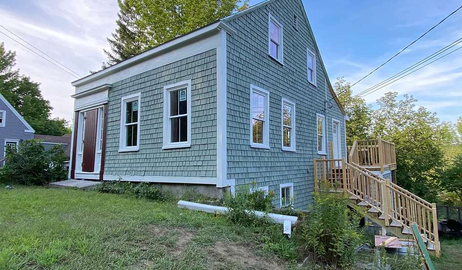 A small blue house with a deck and stairs in front of it.