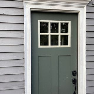 A green door with a white trim is on a gray house.