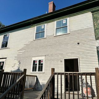 A white house with a wooden deck and stairs leading up to it.