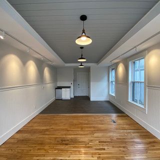 An empty room with hardwood floors , white walls and ceiling lights.